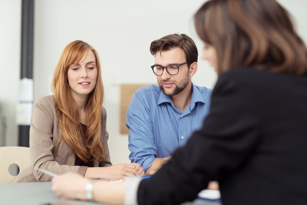 Broker making a presentation to a young couple showing them a document which they are viewing with serious expressions-2